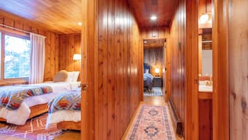 A wooden cabin interior with two beds, a hallway, and a bathroom.