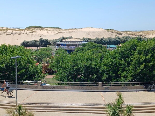A coastal area with a sandy hill, a building with a blue roof, and a cyclist on a path.