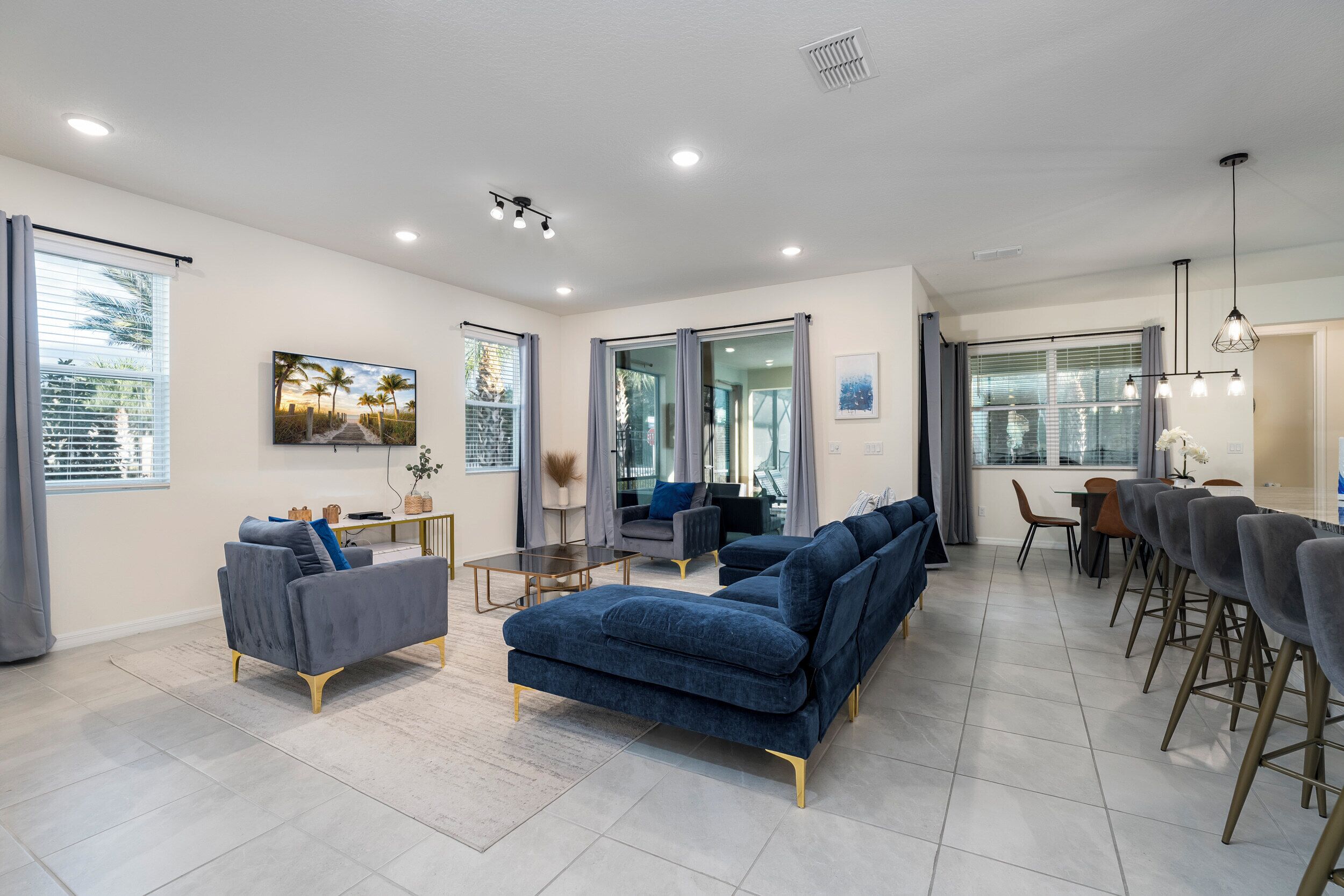 A modern living room with a sofa set, a dining area with chairs, and large windows with curtains.