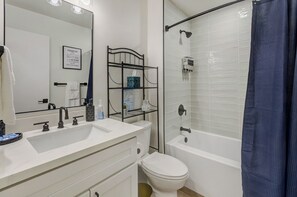 Un baño con un lavamanos blanco, grifos negros, un inodoro, una ducha con puerta de cristal y una cortina de ducha azul.
