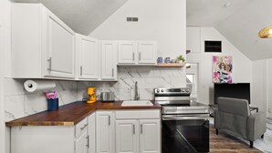 A modern kitchen with white cabinets, a wooden countertop, stainless steel appliances, and a grey sofa in the adjacent living area. - Cozy Loft Apartment in Ohio City (Cleveland)