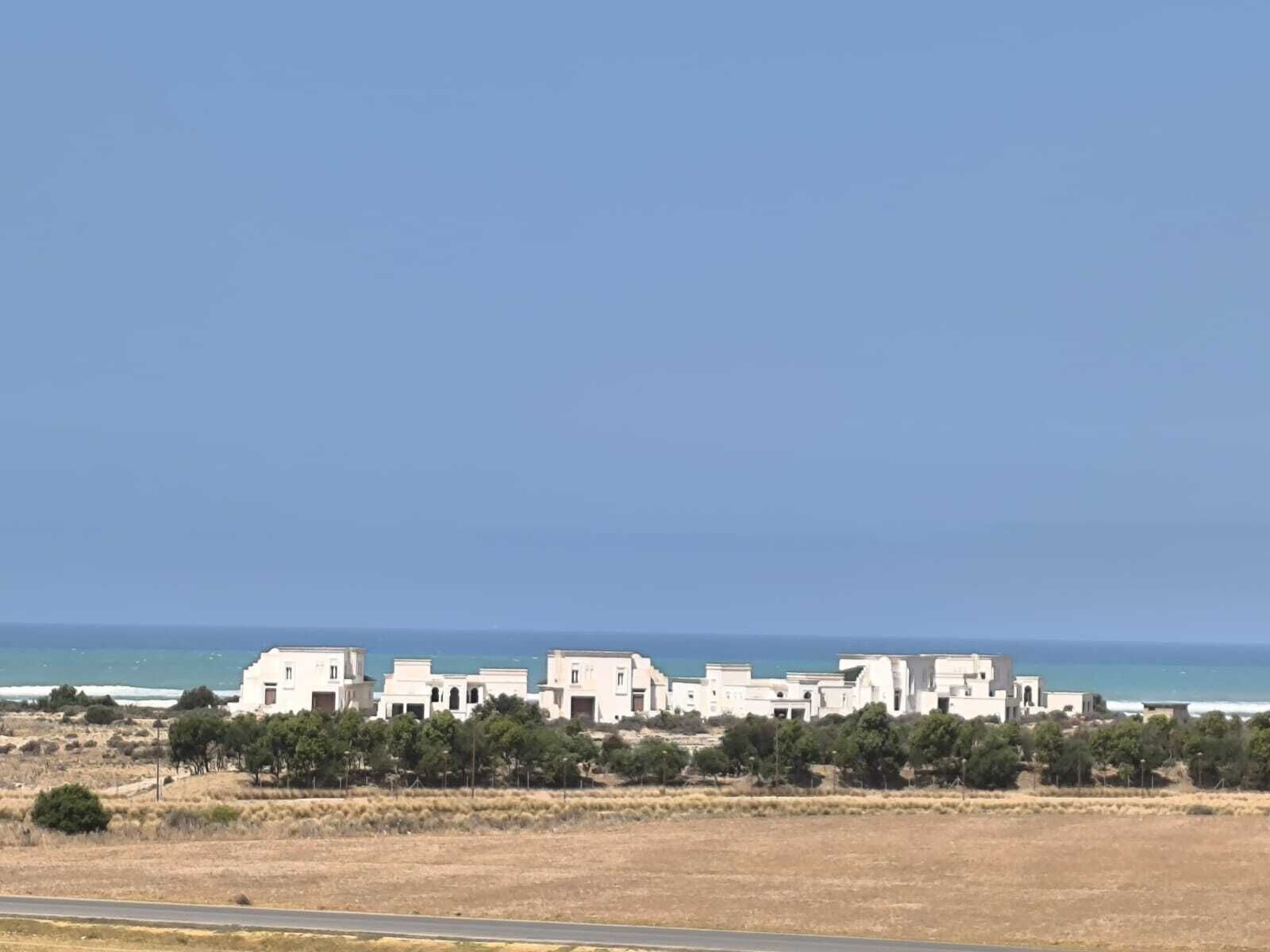 A coastal residential area with white buildings, a clear sky, and a view of the sea.