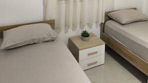 A bedroom with two single beds, a small bedside table with a plant, and sheer curtains on the window. - Seaside Escape – Calm, Safety, and Proximity (طنج ة)