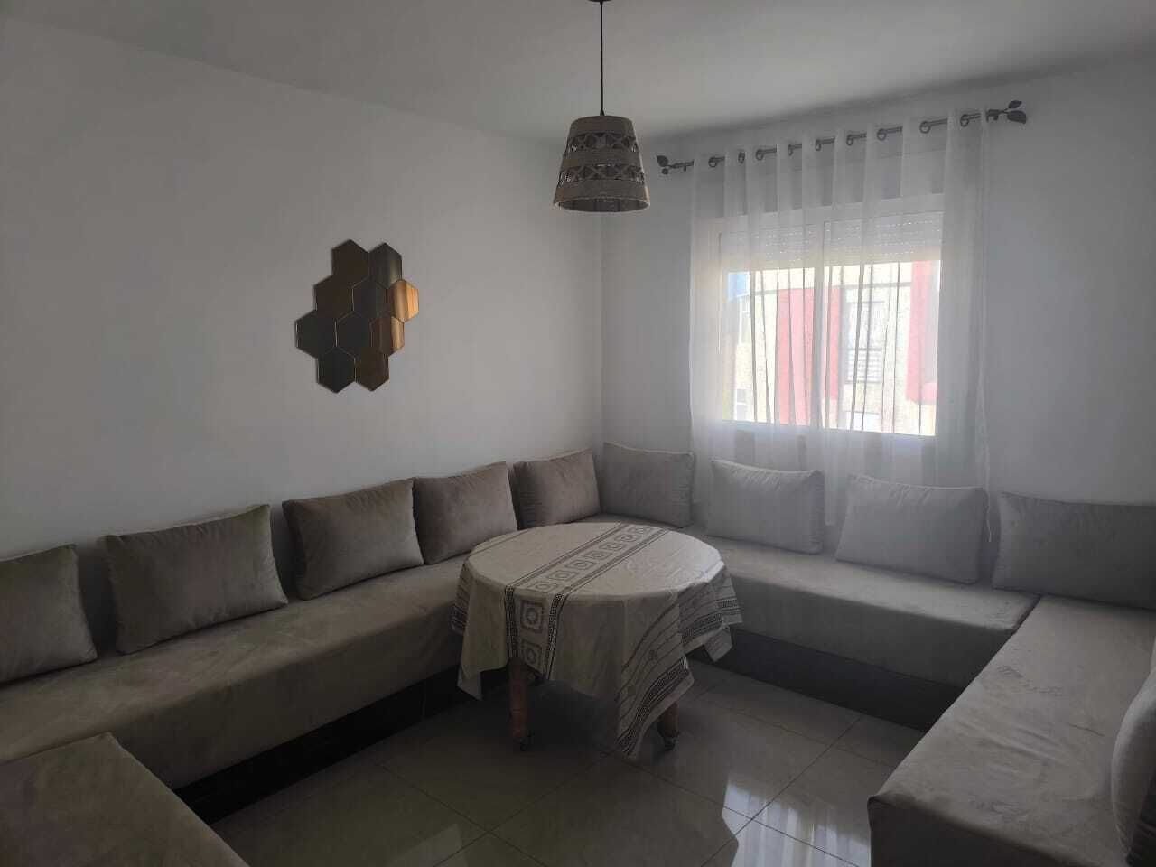 A living room with a sectional sofa, a round table, and a pendant light.
