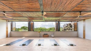 Una habitación amplia con ventanas grandes, techo de madera y esterillas de yoga dispuestas para practicar.
