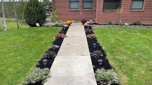 Une allée menant à une maison en briques, avec une pelouse bien entretenue et des parterres de fleurs.