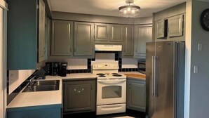 Une cuisine de taille réduite avec des meubles gris, une cuisinière blanche et un réfrigérateur en acier inoxydable.