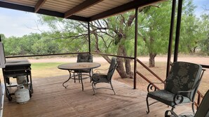 Un patio exterior con una mesa, sillas, una parrilla y un tanque de propano.