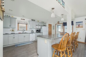 A modern kitchen with white cabinets, a central island with bar stools, and a microwave.