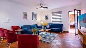 Una sala moderna con un sofá azul, sillas rojas, una mesa de centro y un ventilador de techo.