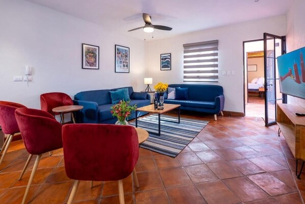 Una sala moderna con un sofá azul, sillas rojas, una mesa de centro y un ventilador de techo.