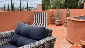 Un patio al aire libre con mobiliario de mimbre, un cojín a rayas y plantas en macetas.