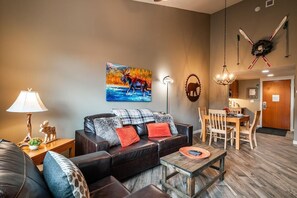 Una sala de estar con sofá, una mesita de centro y un cuadro de un alce.  Hay una zona de comedor con mesa y sillas.
