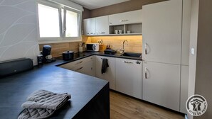 A modern kitchen with white cabinets, a black countertop, and a window providing natural light. - Les Hautes Collières - ECHALAS (ECHALAS)