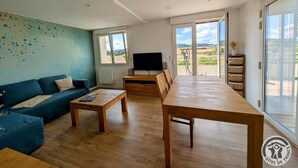 A modern living room with a blue sofa, wooden coffee table, and a TV stand. - Les Hautes Collières - ECHALAS (ECHALAS)