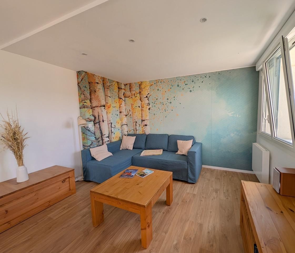 Uma sala de estar moderna com um sofá sectional azul, mesa de centro de madeira e uma janela grande.