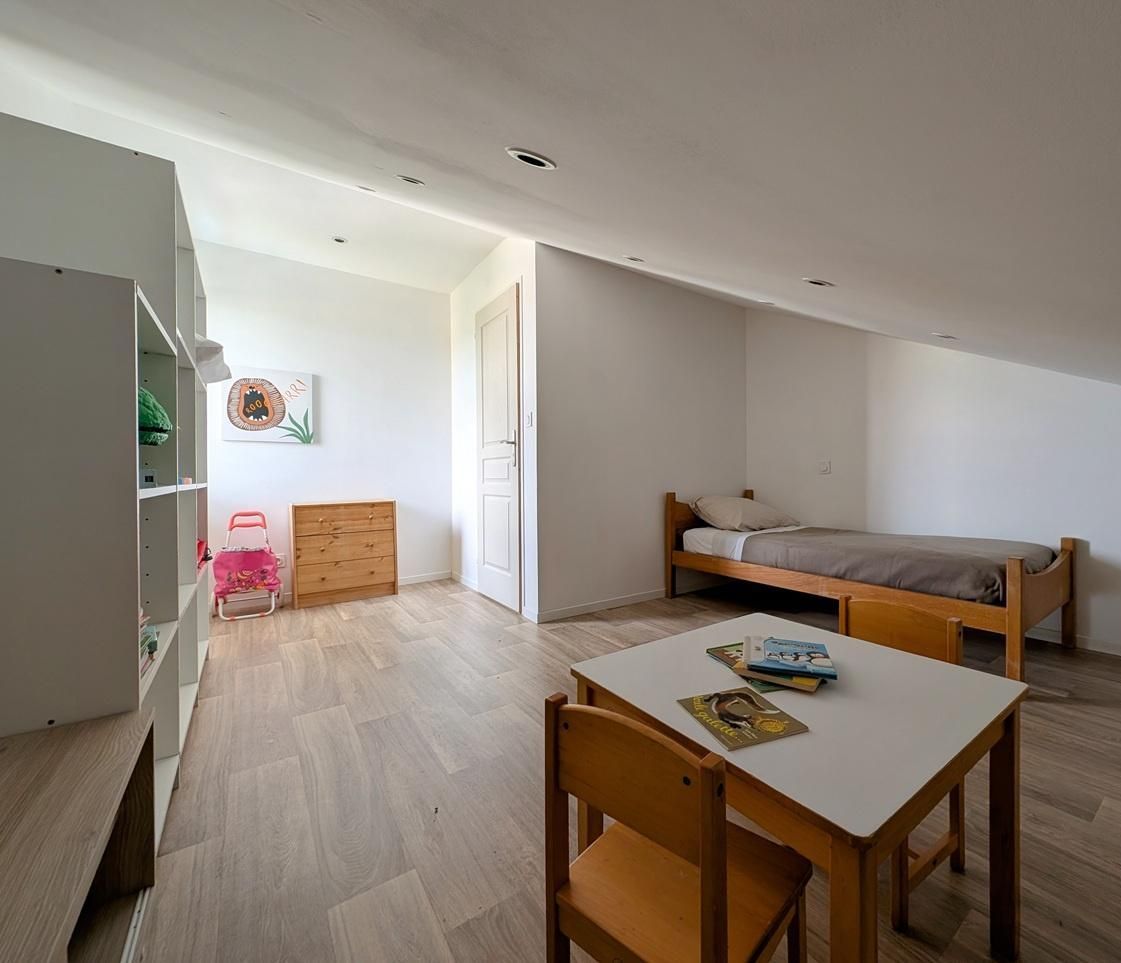Una habitación pequeña y luminosa con una cama, un escritorio con silla, un armario y una puerta que da a otra habitación.