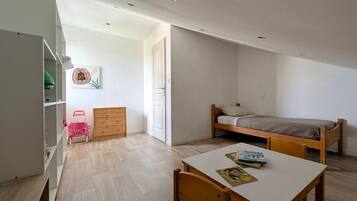 Una habitación pequeña y luminosa con una cama, un escritorio con silla, un armario y una puerta que da a otra habitación.