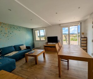 A modern living room with a blue sofa, wooden coffee table, and a TV stand.