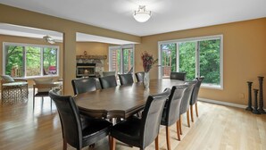 A spacious dining room with a large wooden table surrounded by chairs, large windows, and a fireplace.