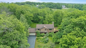 A house surrounded by dense forest with a river in the foreground.