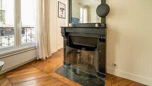Une pièce avec une cheminée, un grand miroir, une fenêtre avec des rideaux et un plancher en bois.