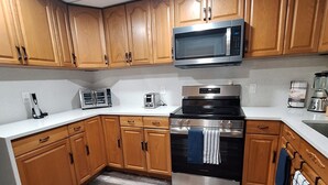 Una cocina con gabinetes de madera, un microondas de acero inoxidable, una estufa a gas y una cafetera.