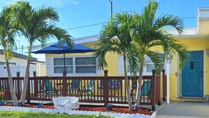 Un barrio residencial con una casa amarilla, una puerta azul y un jardín vallado con palmeras y una estatua blanca.