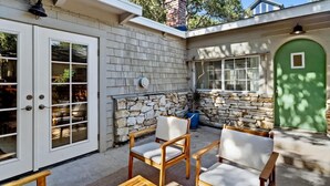 A patio with two wooden chairs and a table, a stone wall, and a green door. - Carmel Cozy Cottage | Room for 4 (Carmel)