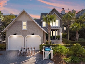 Une maison à deux étages avec un garage, une véranda et un jardin bien entretenu agrémenté de palmiers.