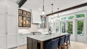 A modern kitchen with a large island, white cabinetry, and a view through large windows. - 30A Dunes by Stay on 30a (Inlet Beach)