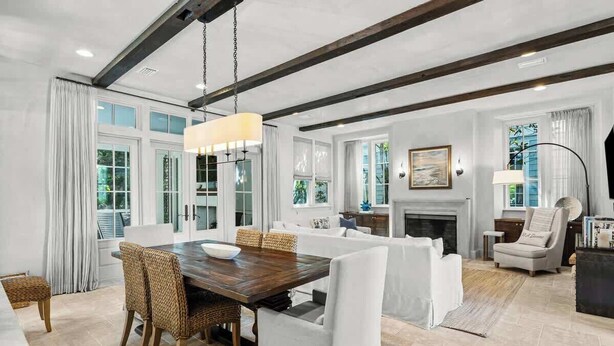 A spacious living area with a wooden dining table, white upholstered chairs, a fireplace, and large windows. - 30A Dunes by Stay on 30a (Inlet Beach)