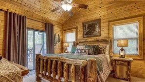 A log cabin bedroom with a wooden bed, a ceiling fan, and a window with blinds.