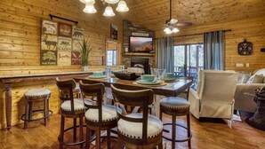 A rustic wooden interior with a dining area, a fireplace, and a television.