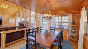 A cozy cabin interior with a wooden dining table, chairs, a sofa, and a fireplace. - 4BR Pigeon Forge Cabin | Hot Tub, Sauna, Game Room | 1 Mi to Dollywood, Pool Access, Scenic Views (Pigeon Forge)