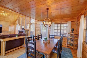 Un interior de cabaña acogedor con una mesa de comedor de madera, sillas, un sofá y una chimenea.