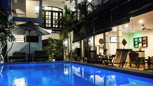 A swimming pool with lounge chairs and umbrellas, surrounded by indoor plants and a bar area. - Spacious 5-bedroom house with private pool (Siem Reap Province)