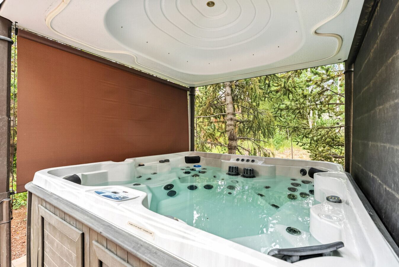 Ein Whirlpool mit mehreren Düsen, umgeben von einer Holzterrasse und einem braunen Sonnensegel.