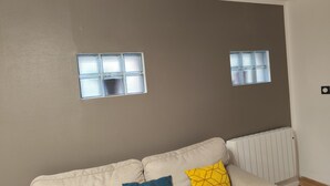 A living room with a beige sofa, two windows, and a radiator. - Charming 25m2 studio close to CDG airport, Parc Astérix, sandy sea, (Louvres)
