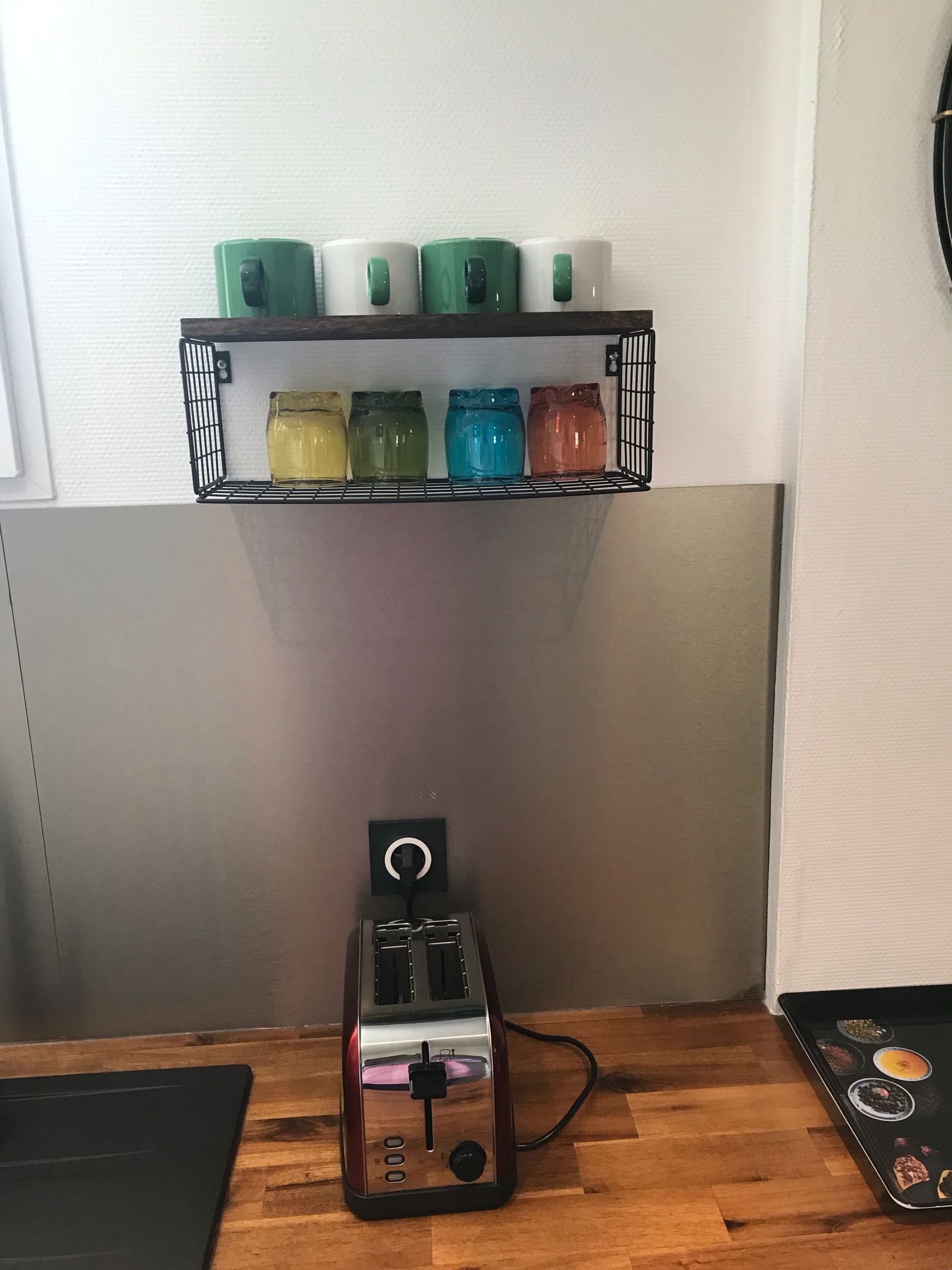Eine Küche mit einem Toaster auf der Arbeitsfläche, einem Regal mit Gläsern und einem an der Wand befestigten Lichtschalter.