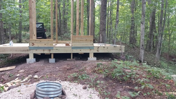 Un sitio de construcción con una plataforma de madera sostenida por pilares de hormigón, rodeado por un bosque.