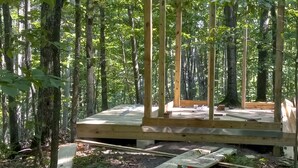 Una terraza de madera en un área boscosa, con árboles en el fondo.