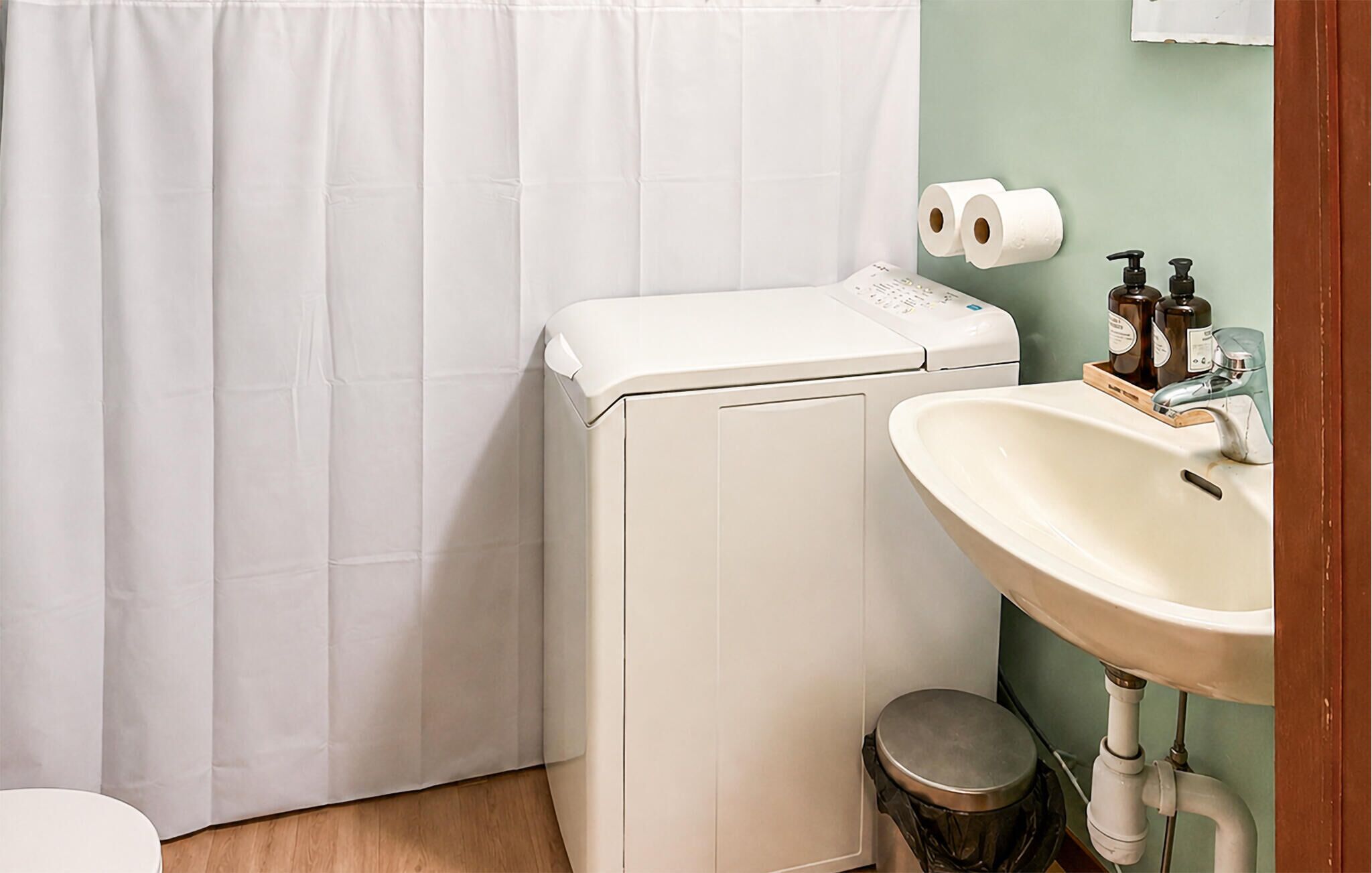 A bathroom with a white toilet, a white washing machine, a sink, and a shower curtain.