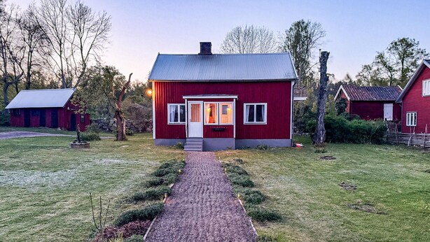 Una casa roja con un camino de grava que conduce a la entrada, rodeada de árboles y un cielo despejado.