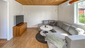 Una sala de estar moderna con un sofá seccional, una mesita redonda, un televisor y un mueble de madera.