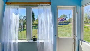 Una habitación con ventana, puerta y vistas a una casa y follaje.