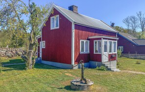 A red wooden house with a sloped roof, a small porch, and a stone wall in the background.