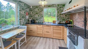A kitchen with wooden cabinets, a black countertop, a window with a view of a garden, and a hanging light fixture. - Stunning home in Sjötofta with sauna (Sjötofta)