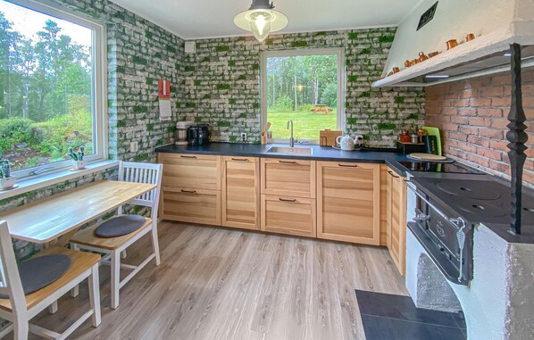 A kitchen with wooden cabinets, a black countertop, a window with a view of a garden, and a hanging light fixture.