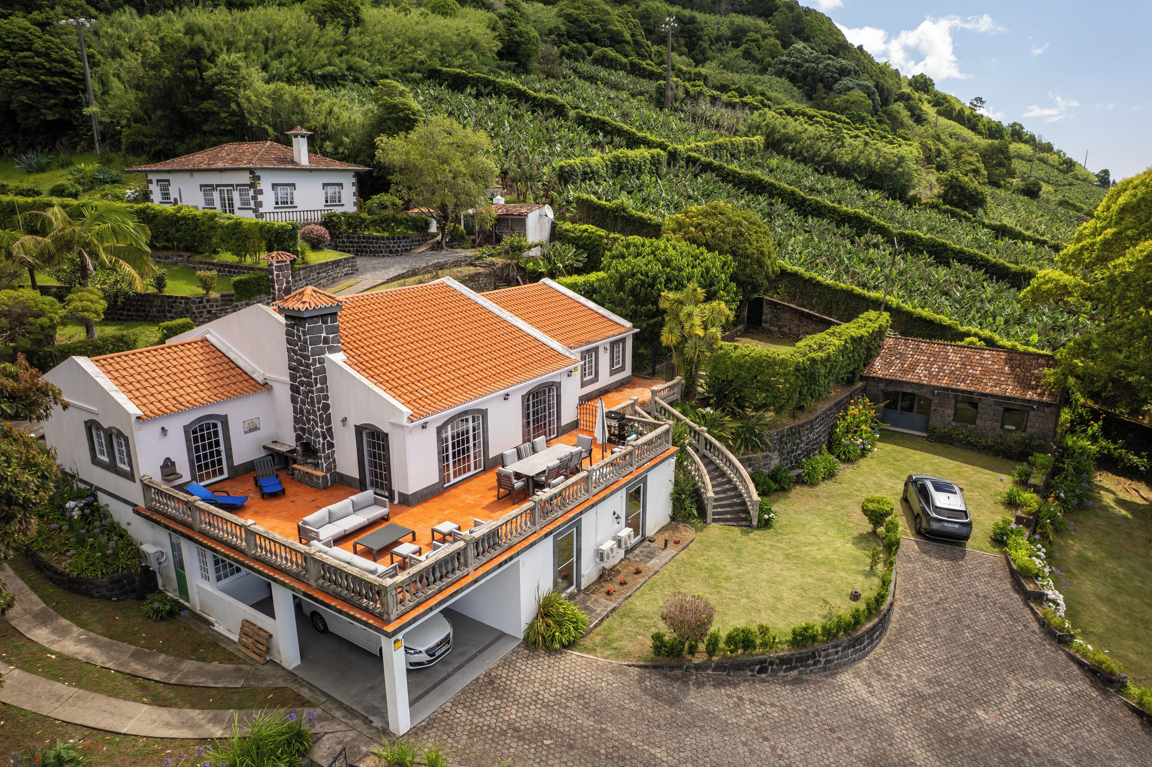 A large house with a spacious patio, a stone chimney, and a car parked in the driveway.